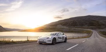 Tesla sur une route devant lac et forêt