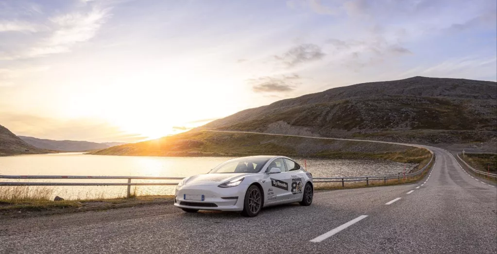 Tesla sur une route devant lac et forêt