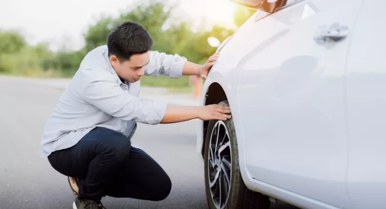 homme qui vérifie ses pneus de voiture